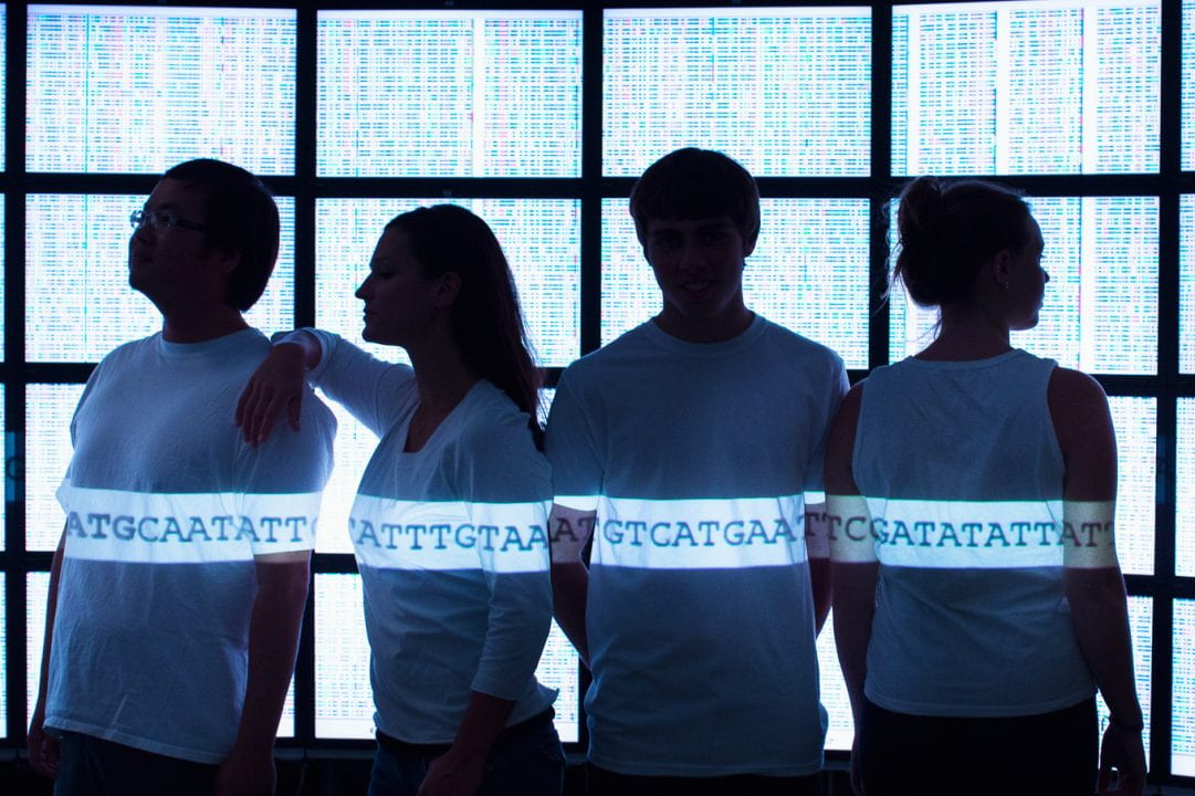 Four people standing in a row with a string of As, Ts, Cs, and Gs illuminated on their shirts.
