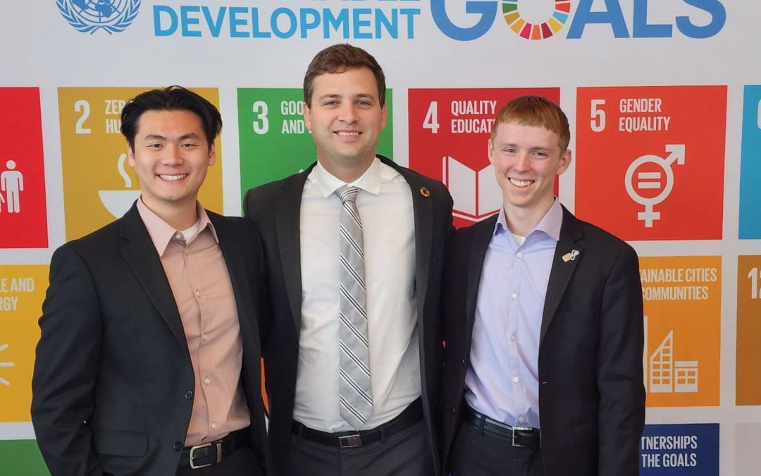 Adriano standing with two other young men in front of a backdrop that reads "sustainable development goals"