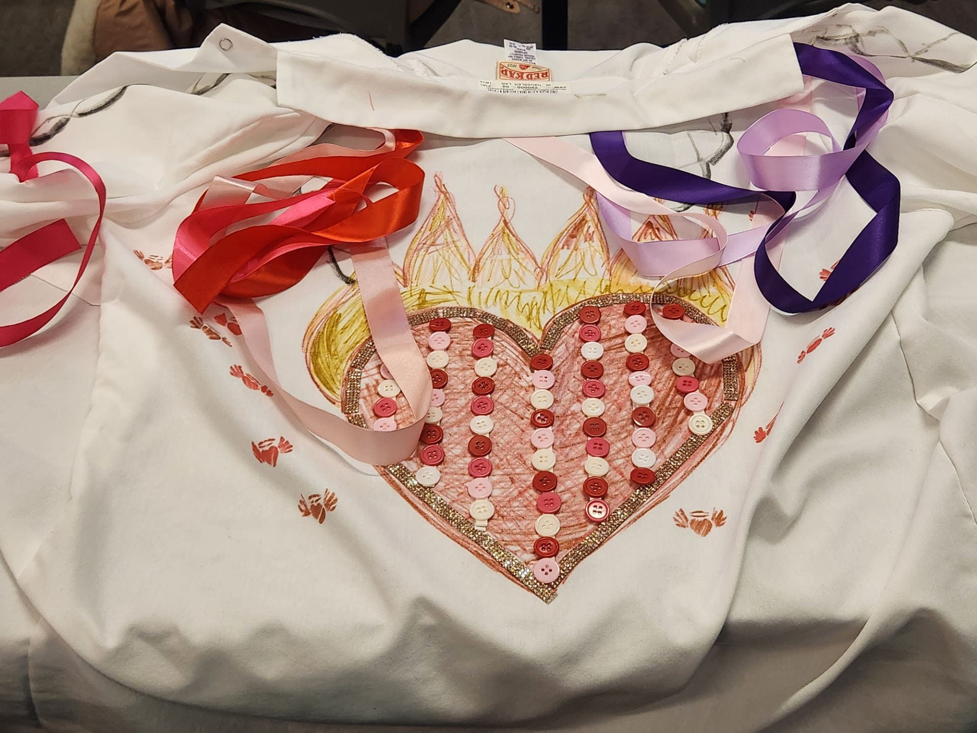 A lab coat decorated with a flaming heart on the back. The heart is filled in with red and white buttons.